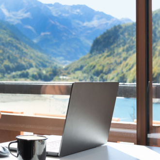 Laptop image with a coffee mug next to it. In the background is a window with mountains.