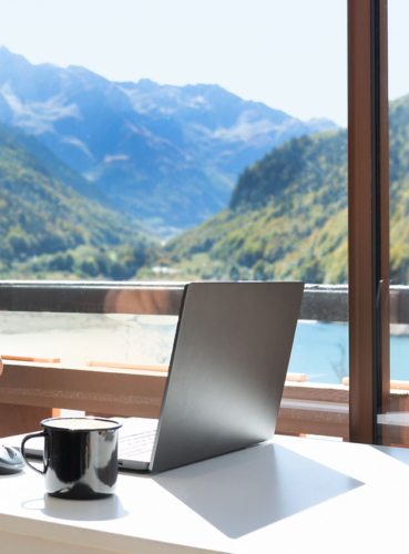 Laptop image with a coffee mug next to it. In the background is a window with mountains.
